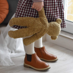 Child holding a teddy bear in a room with a window and pumpkin decoration.
