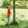 Child in an orange shirt climbing a tree in a grassy area