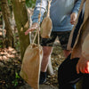 Person holding a beige drawstring bag in a forest setting