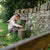 Child playing with a wooden stick near a stone wall in a garden
