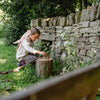 Child playing with a wooden stick near a stone wall in a garden