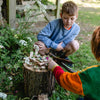 Two children playing with a fairy garden on a tree stump in a garden setting.