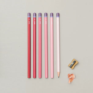 Set of red and pink pencils with a sharpener on a gray background