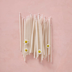 White candles with small flowers arranged on a pink background