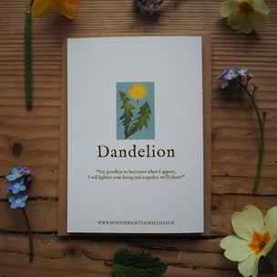 Card with dandelion illustration and text on a wooden surface with flowers