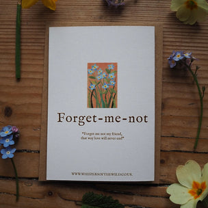 Note with 'Forget-me-not' design and text on a wooden surface with flowers