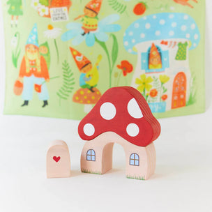 Wooden mushroom-shaped house toy with a small door on a white surface, with a colorful children's book in the background.
