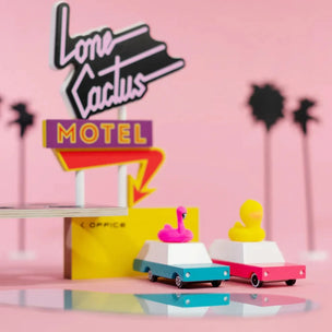 Candylab wooden toy wagons one with a pink flamingo on the roof the other with a yellow duck, in front of a motel | Conscious Craft