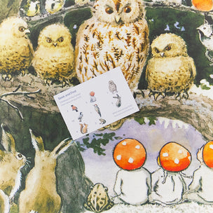 A close-up of a printed fabric or wallpaper pattern featuring a woodland scene with several owls, a rabbit, mushrooms, and a small card labeled 'Beak and Feed' placed on top.