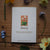 Card with daisy illustration and text on a wooden surface with flowers