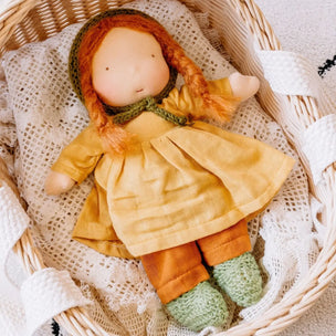 Toy doll with red hair and a yellow dress in a wicker basket with a white lace cloth.