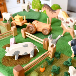 Wooden farm animals and tractor on a green felt play mat