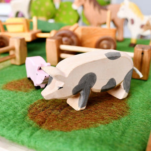 Wooden pig toy on a green felt surface with other toys in the background