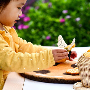 Child in a yellow sweater holding a felted bee with a blurred garden background