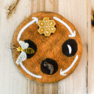 Round felt board with embroidered bee, flower, and honeycomb on a wooden surface