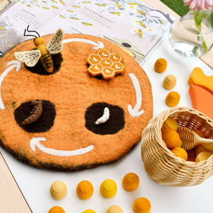 Round felt board with a bee and honeycomb design, surrounded by small round felt pieces on a white surface.