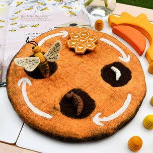 Round orange felt board with bee and honeycomb decorations on a white surface.