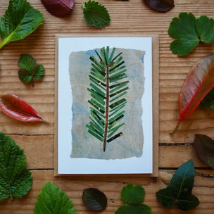 Card with a leaf design surrounded by real leaves on a wooden surface