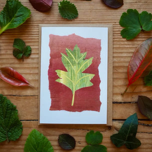 Card with leaf design surrounded by real leaves on a wooden surface