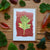Card with leaf design surrounded by real leaves on a wooden surface