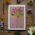 Floral illustration herb Robert on a pink background with real flowers around on a wooden surface