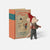 A small Maileg mouse figurine wearing a red hat and striped scarf stands beside a vintage-style hardcover book titled "Christmas Tales: Bedtime Stories" on a light gray background.