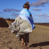 Person walking on a beach with a colorful towel draped over their shoulders