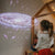 Child looking at a projected image of a galaxy in a room with a wooden house-shaped frame.