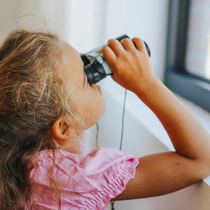 Child looking through binoculars by a window