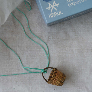 Small woven basket with a string on a textured surface with 'KRAUL' branding in the background.