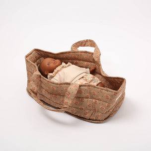 Baby doll in a floral-patterned bassinet on a white background