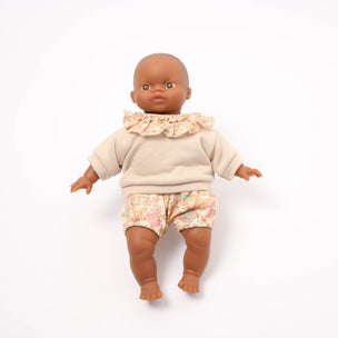 Baby doll wearing a beige outfit with a ruffled collar and floral shorts on a white background