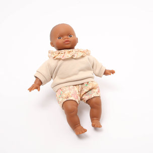 Baby doll wearing a beige sweater and floral shorts on a white background