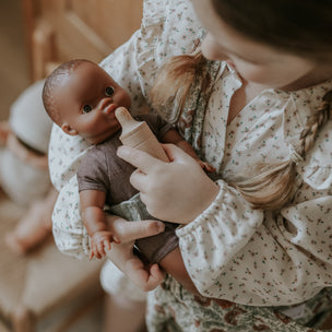 Child holding a baby doll with a bottle in a home setting