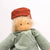 Toy figure with a red hat and green shirt standing on a wooden arch against a white background