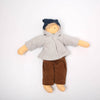 Doll wearing a gray coat, brown pants, and a blue hat on a white background