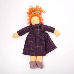 Doll with orange hair wearing a purple plaid dress on a white background
