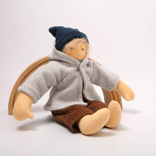 Small doll wearing a gray coat, brown pants, and a blue hat on a white background