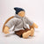 Small doll wearing a gray coat, brown pants, and a blue hat on a white background