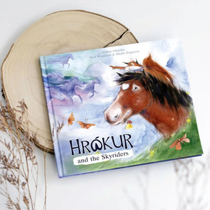 Children's book titled 'Hrökur and the Skyriders' with a horse illustration on a wooden surface.