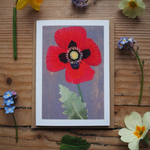 Card with a red flower design on a wooden surface with surrounding flowers.