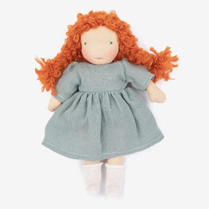 A handmade cloth doll with curly orange-red hair, a dusty blue dress, and white socks, photographed against a clean white background.