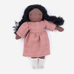 A handmade fabric doll with dark brown skin, long black curly hair, and a dusty pink dress, paired with white knit socks, shown against a plain white background.