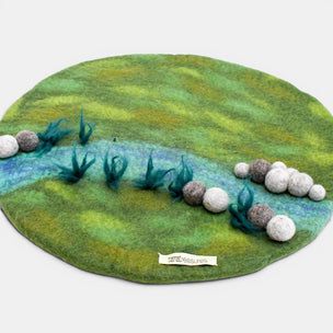 Felted landscape with green grass, blue water, and gray rocks on a white background