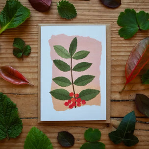 Card with leaf and berry design surrounded by real leaves on a wooden surface