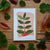 Card with leaf and berry design surrounded by real leaves on a wooden surface