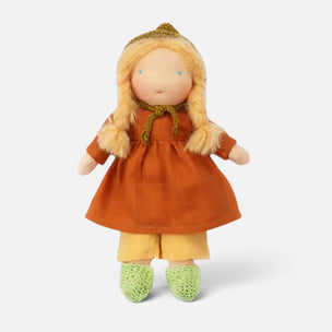 A handmade fabric doll with long blonde braided hair, wearing an orange dress, yellow pants, green crocheted shoes, and a gold bonnet, set against a plain light gray background.