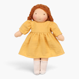 A soft fabric doll with curly reddish-brown hair, wearing a mustard yellow dress and cream-colored socks, photographed against a clean white background.