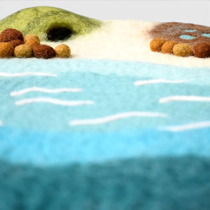 Artistic depiction of a beach scene with green hills and brown rocks.