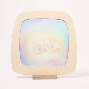 A square wooden toverlux window frame with rounded corners and a small wooden easel stand, featuring a pastel watercolor painting of a white figure in a circular pose against a soft blue, yellow, and pink background.